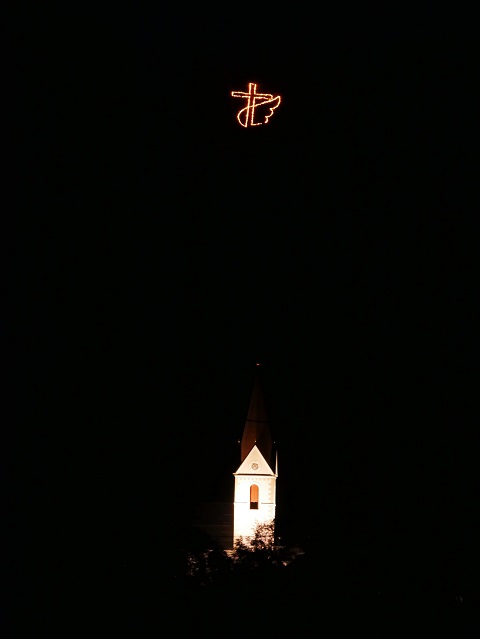 geflügeltes Feuerkreuz über dem Kirchturm von Schattwald